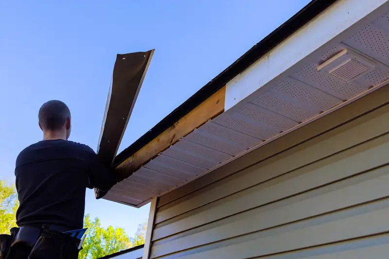 A professional contractor performing soffit repair on a house, replacing old materials to improve ventilation and protection.